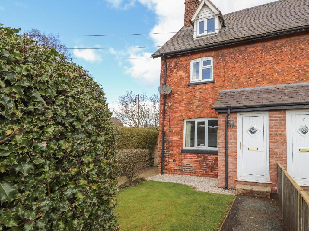 a brick house with a white door and a yard at 1 Organsdale Cottages in Kelsall Hill