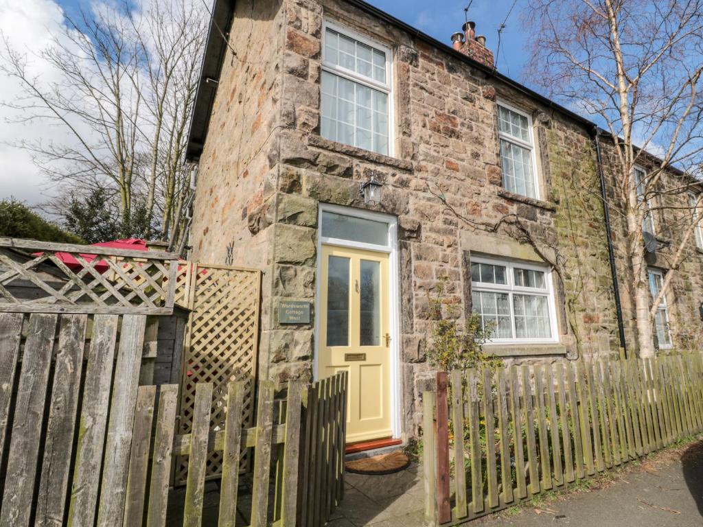 a brick house with a yellow door and a fence at Wordsworth Cottage West in Morpeth