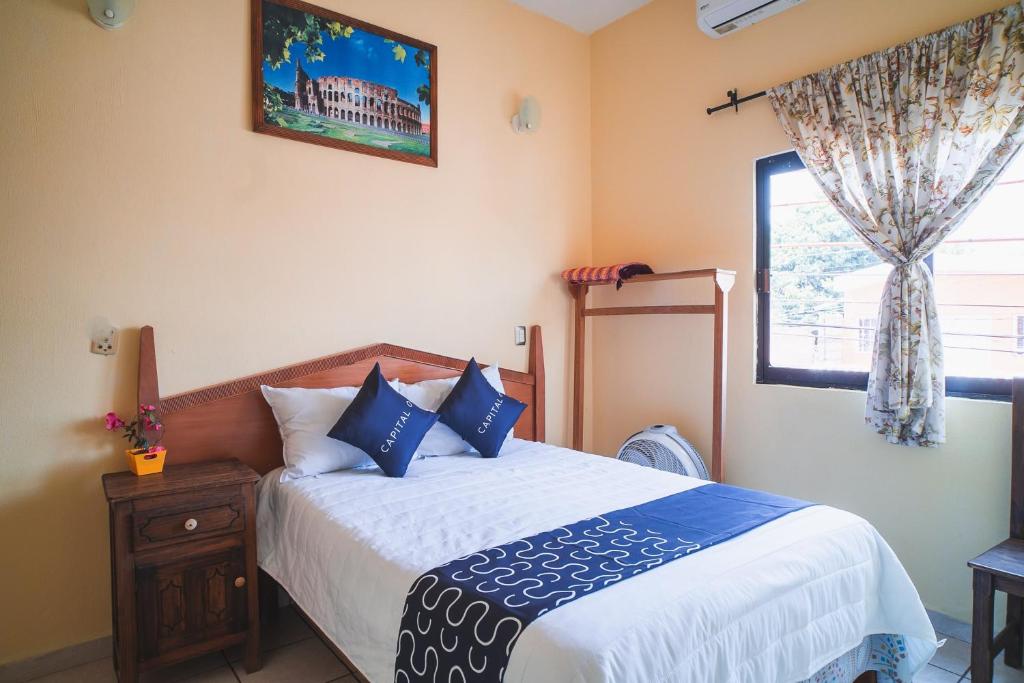 a bedroom with a bed with blue pillows and a window at Capital O Hotel Aurora, Tuxtla Gutiérrez in Tuxtla Gutiérrez