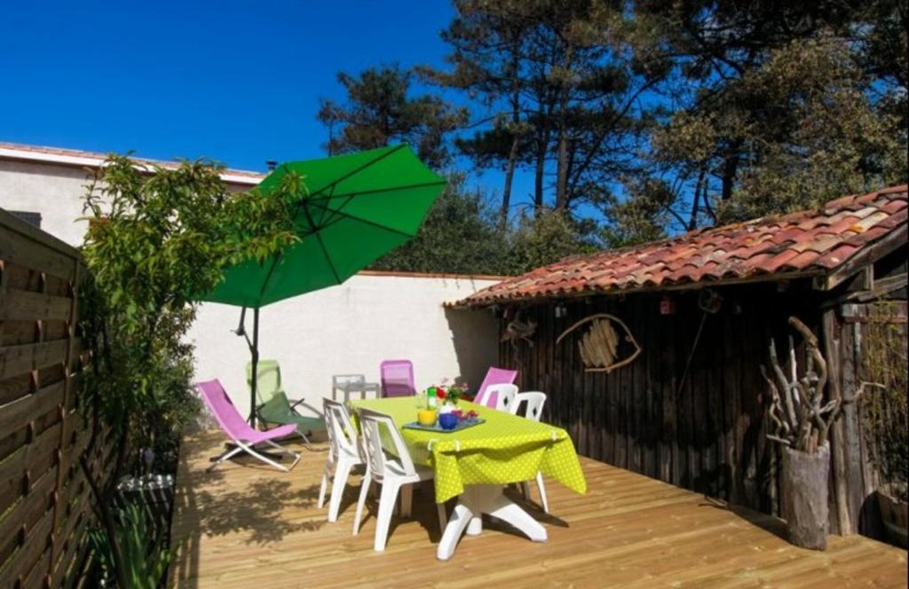 einen Tisch und Stühle mit einem grünen Regenschirm auf einer Terrasse in der Unterkunft Nice House near the beach, beautiful garden and terrace in Hourtin