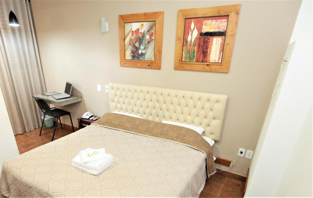 a bedroom with a bed and a desk with a laptop at Hotel Pouso Novo in Matão