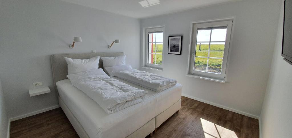 Un dormitorio con una cama blanca con dos ventanas. en Ferienhaus Südwesthörn, en Emmelsbüll-Horsbüll