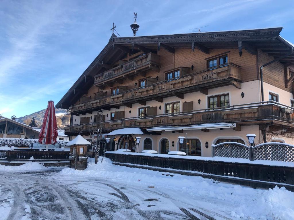 un gran edificio de madera con nieve delante en Ferienhotel Alpenhof en Aurach bei Kitzbuhel