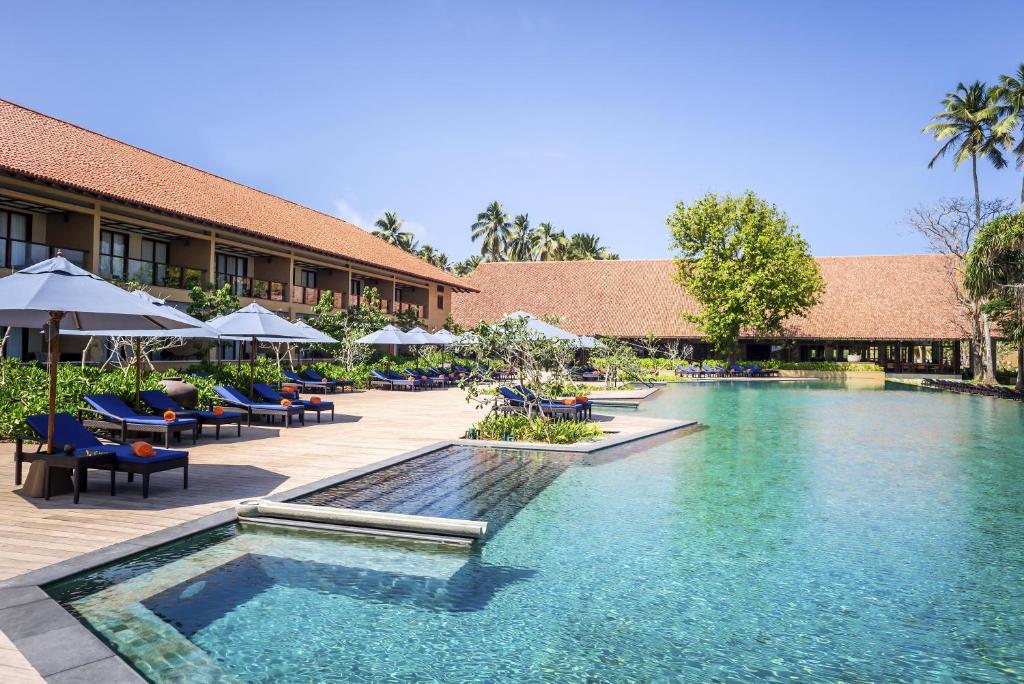 a patio with a pool, chairs, and tables in it at Anantara Kalutara Resort in Kalutara