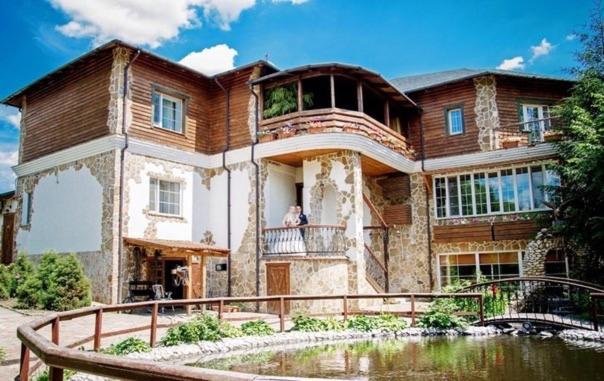 a large house with a pond in front of it at Hotel Orlinoye Gnezdo in Subottsi