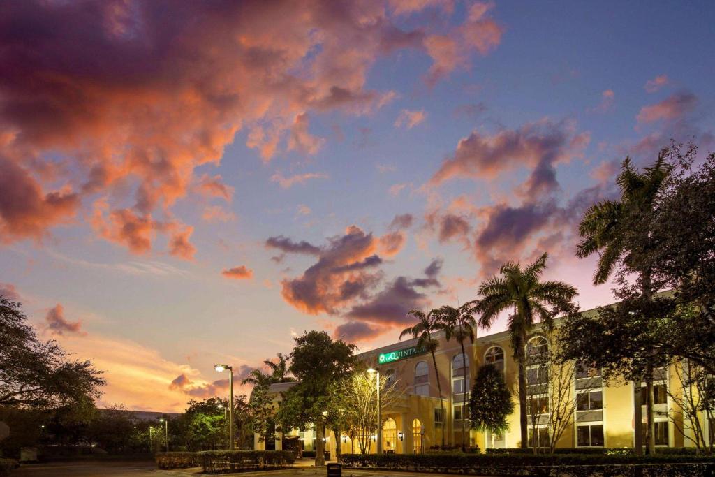 a building with palm trees and a cloudy sky at La Quinta Inn & Suites by Wyndham Sunrise in Sunrise