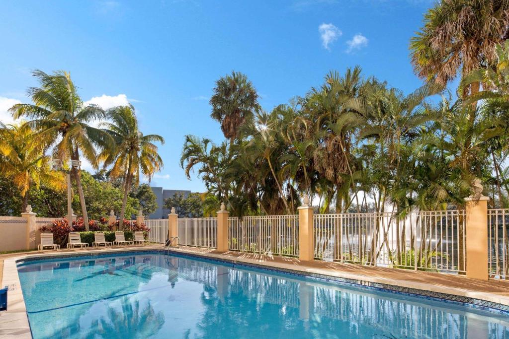a swimming pool with palm trees and a fence at La Quinta Inn & Suites by Wyndham Sunrise in Sunrise