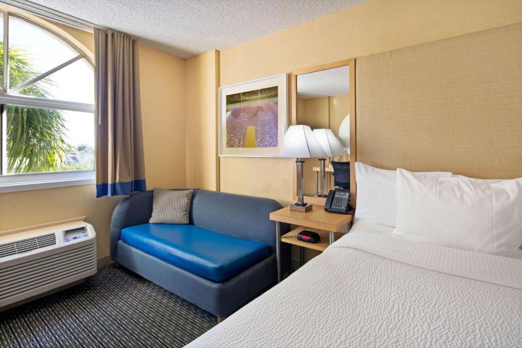 a hotel room with a bed and a blue chair at La Quinta Inn & Suites by Wyndham Sunrise in Sunrise