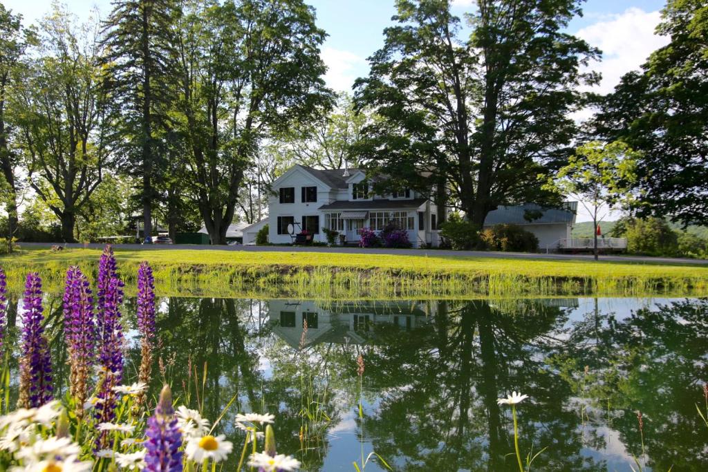 une maison reflétée dans un étang fleuri dans l'établissement Enfield Manor Bed&Breakfast and Vacation Rental, à Newfield