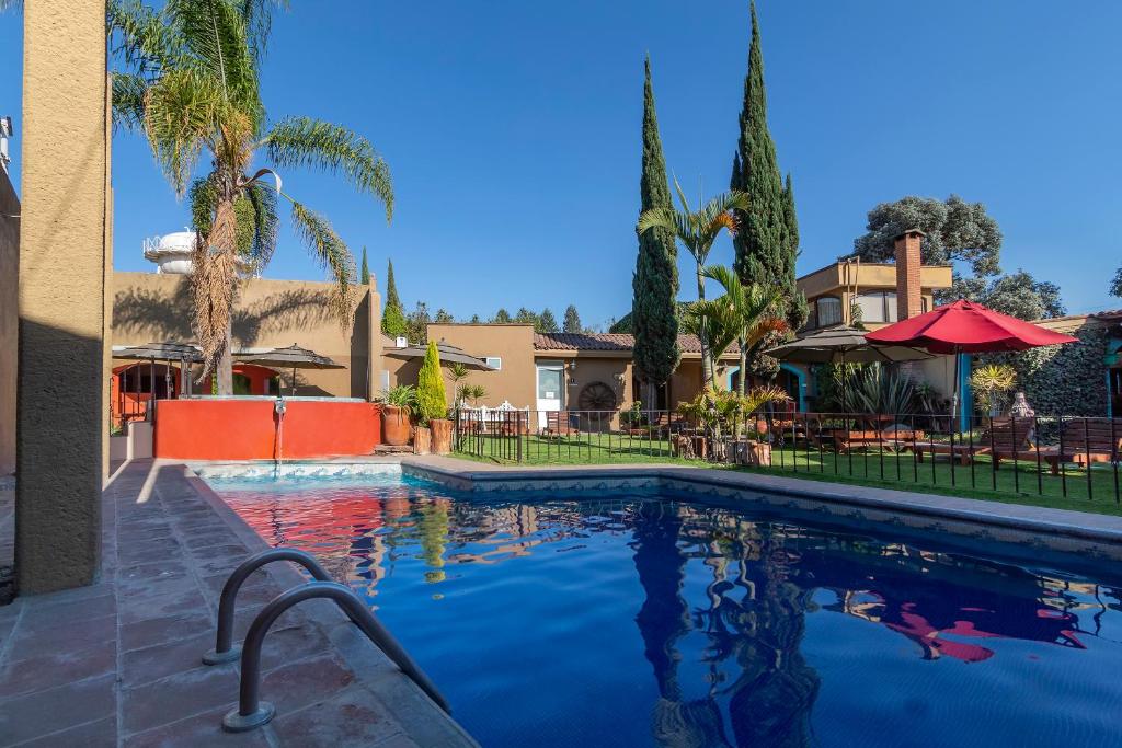 una piscina con palmeras y una casa en Capital O La Huerta Golf & Hotel, en Cholula