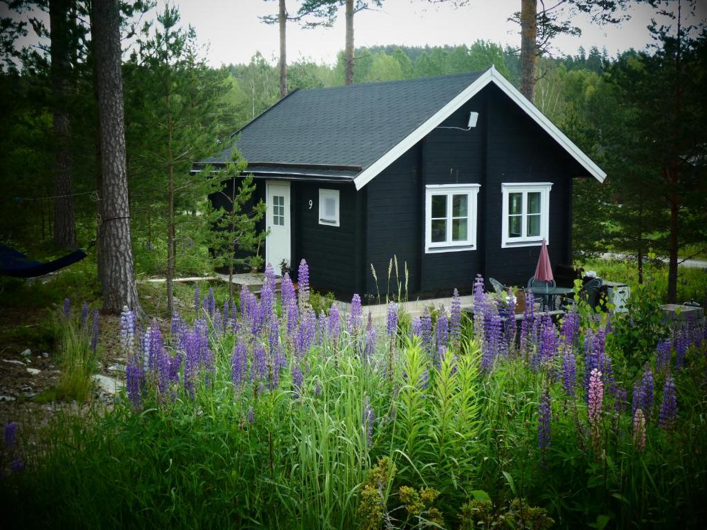 uma casa preta com flores roxas em frente em Fröya Timber Cottage em Arvika