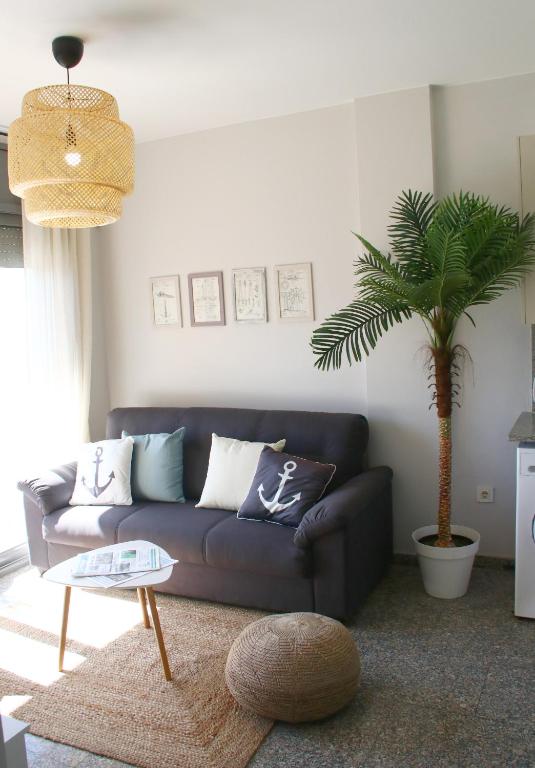 a living room with a couch and a palm tree at SeaHomes Vacations, BEACH&POOL, in Fenals Beach in Lloret de Mar