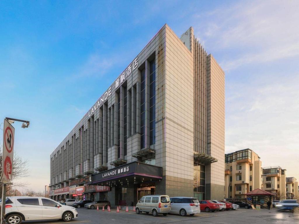 a large building with cars parked in a parking lot at Lavande Hotel (Tianjin Zhongbei Avenue) in Tianjin