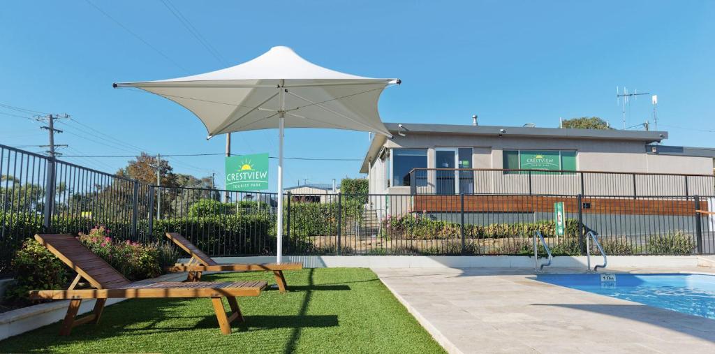 eine Terrasse mit zwei Bänken und einem Sonnenschirm neben einem Pool in der Unterkunft Crestview Tourist Park in Queanbeyan