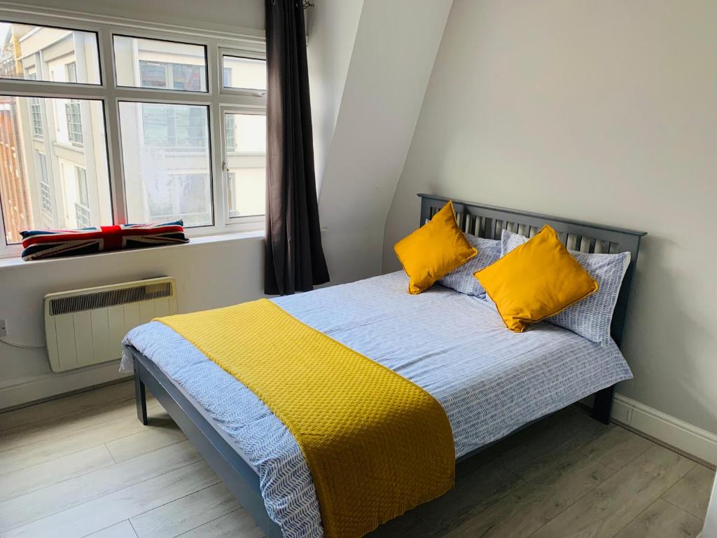 a bedroom with a bed with yellow pillows and a window at X Farringdon Apartments in London