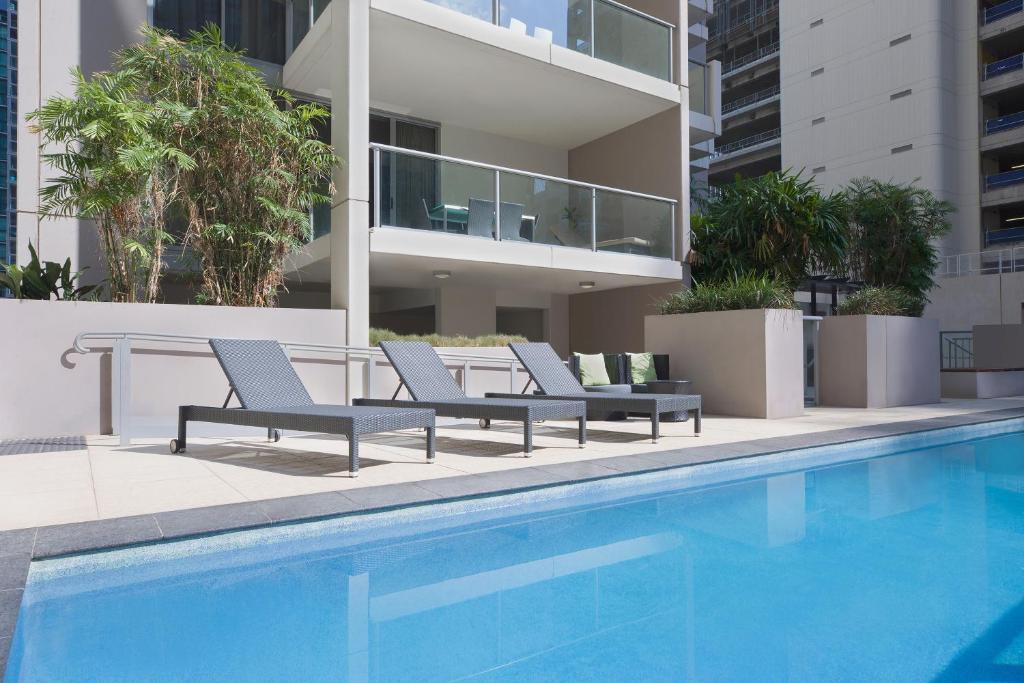 een zwembad met 2 ligstoelen naast een gebouw bij Mantra Midtown in Brisbane