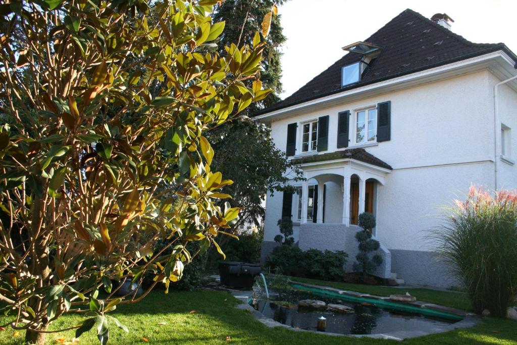 une maison blanche avec un arbre en face dans l'établissement Gästehaus am Weiher, à Weil am Rhein