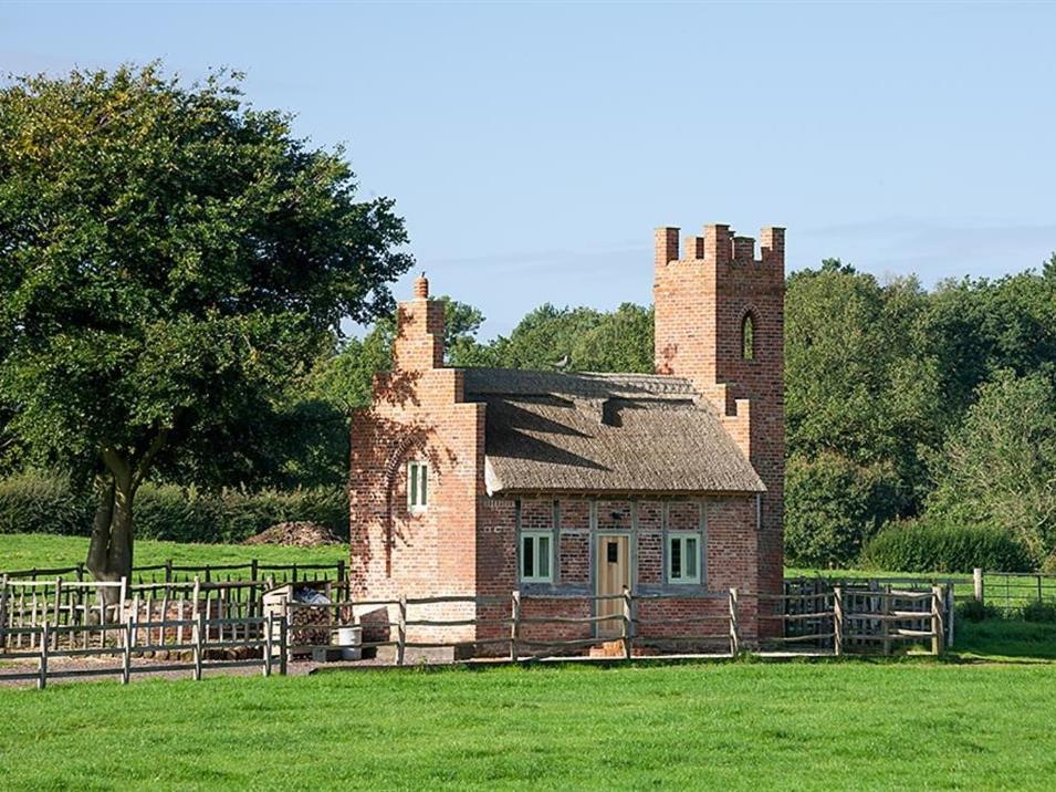 an old brick building with a tower in a field at The Shooting Folly in Cheswardine