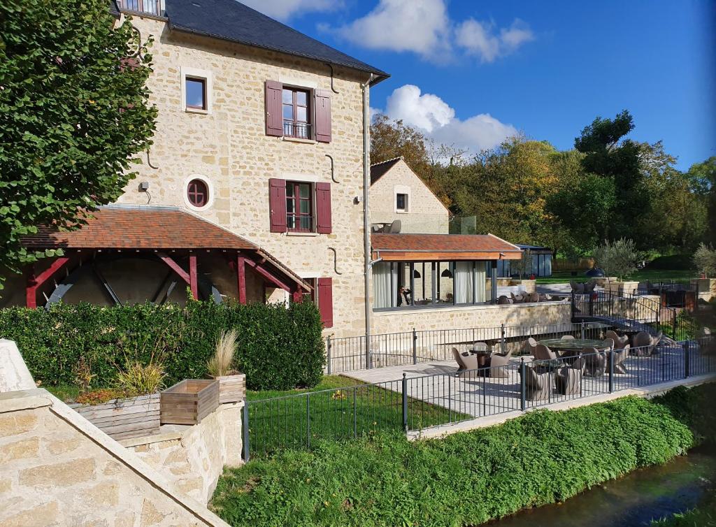 a large building with chairs and a river in front of it at Le Moulin des Marais in Gaillon-sur-Montcient