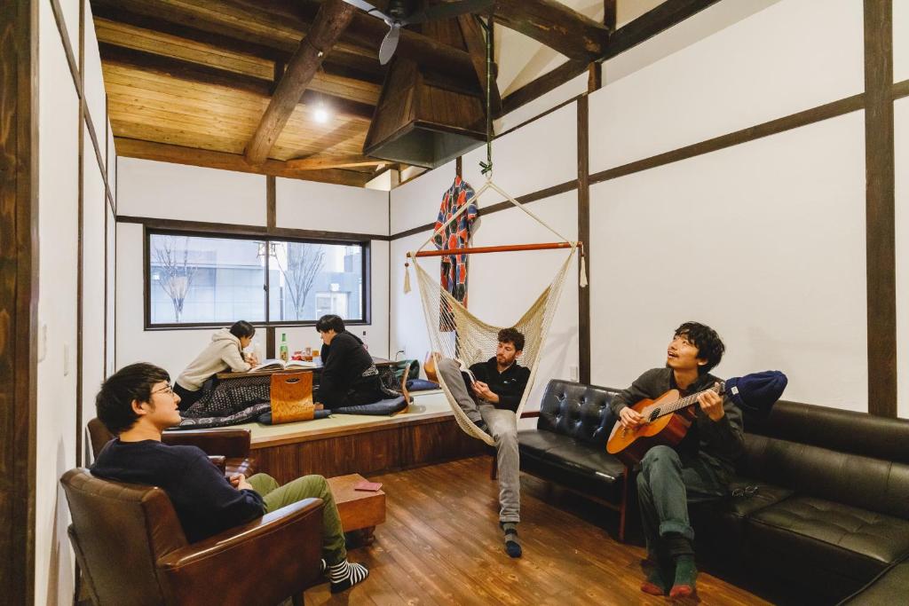 a group of people sitting in a room playing guitar at Couch Potato Hostel in Matsumoto