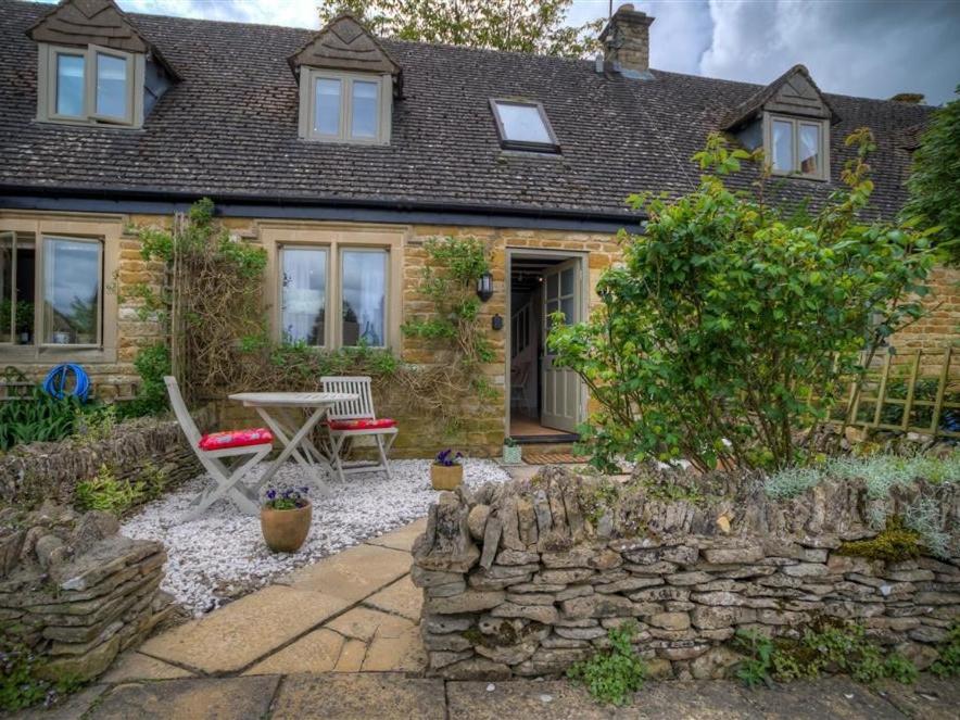 a brick house with a stone wall and a patio at Bobble Cottage in Bourton on the Water