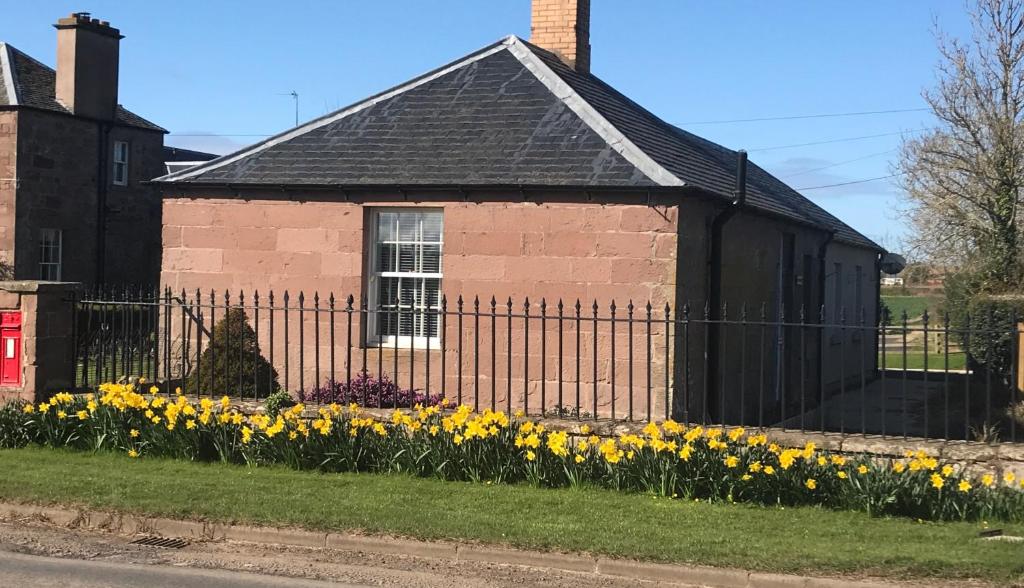 a house with a fence and flowers in front of it at The West Lodge -dog friendly, cosy, Scottish Borders cottage in Berwick-Upon-Tweed