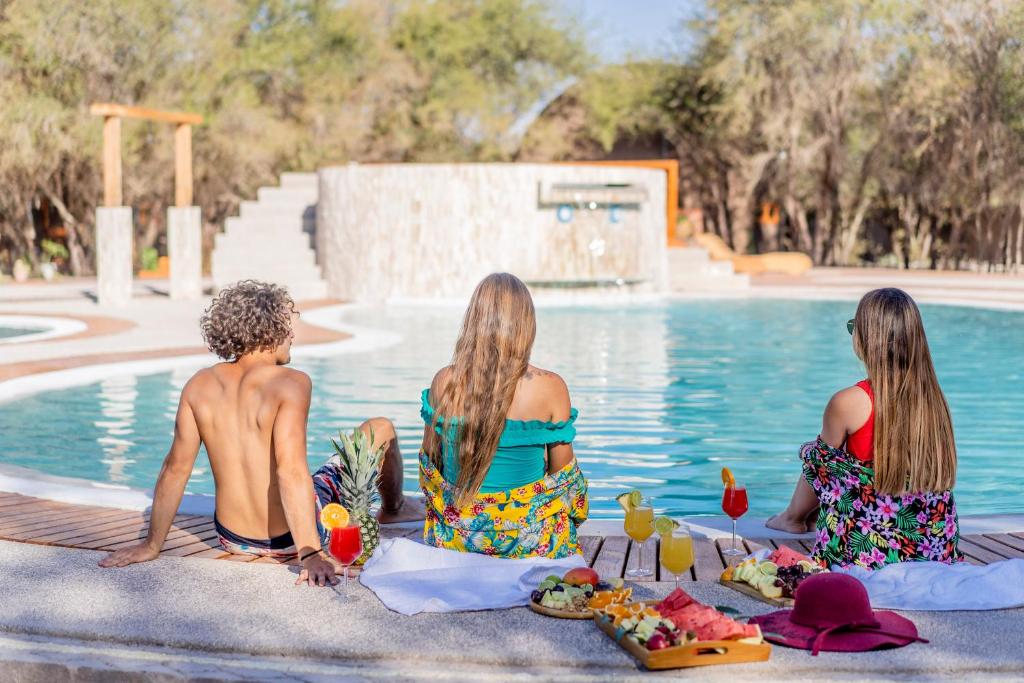 un grupo de tres chicas sentadas junto a una piscina en Tantakuy Eco Experience Hotel en La Huaica