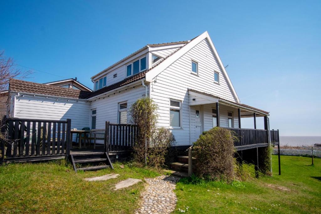 a white house with a porch next to the ocean at Shore Cote, Thorpeness in Thorpeness