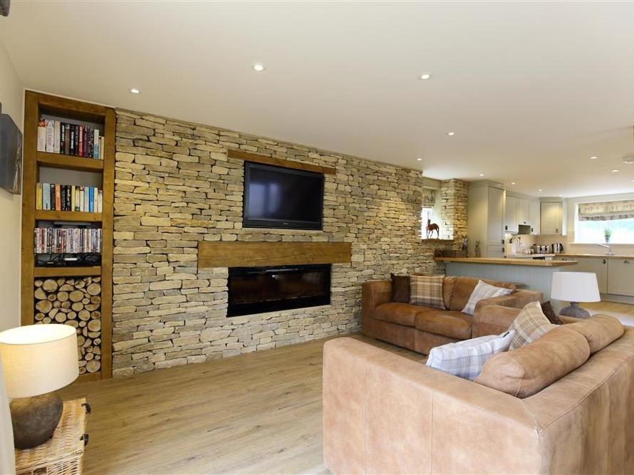 sala de estar con sofá y chimenea de piedra en Old Groom's Cottage, en Witney