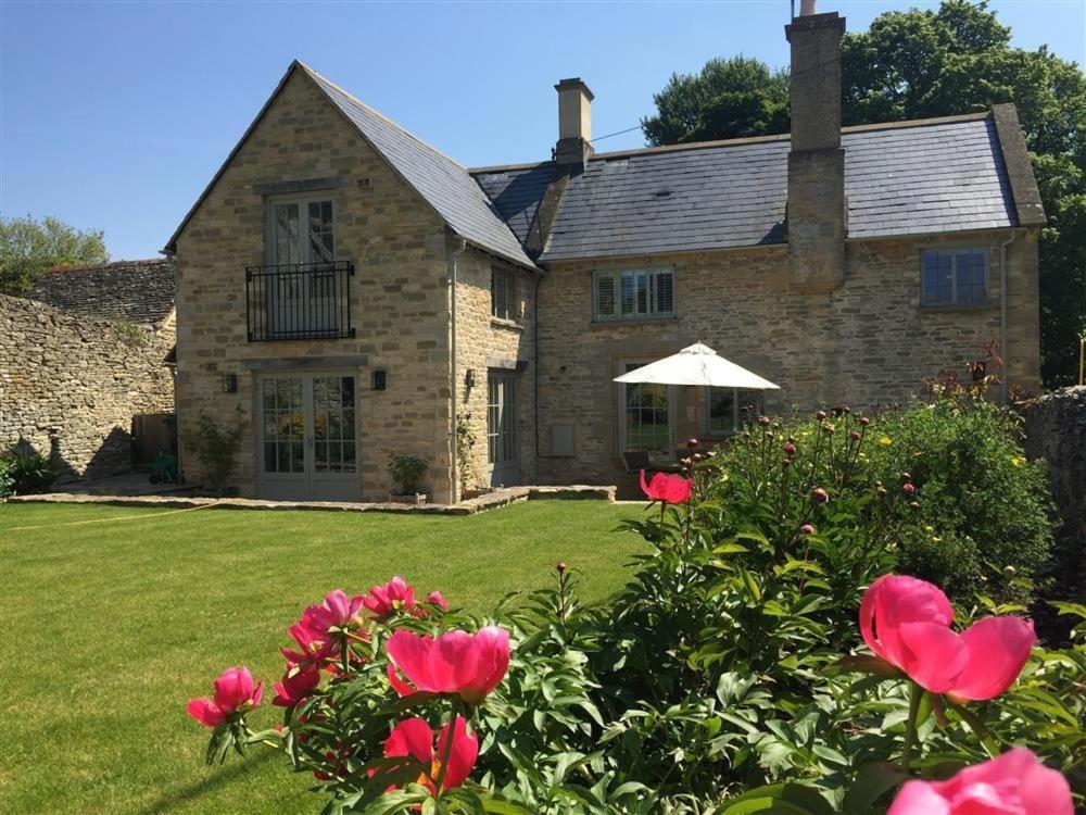 a stone house with pink roses in front of it at Hillside Cottage in Burford