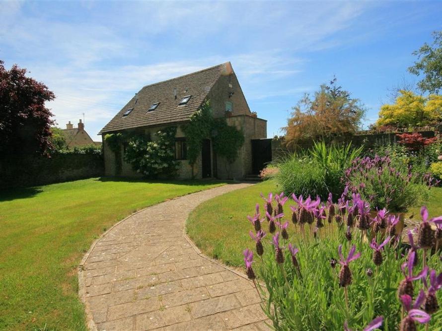 a brick path leading to a house with purple flowers at Temple Mews in Stow on the Wold