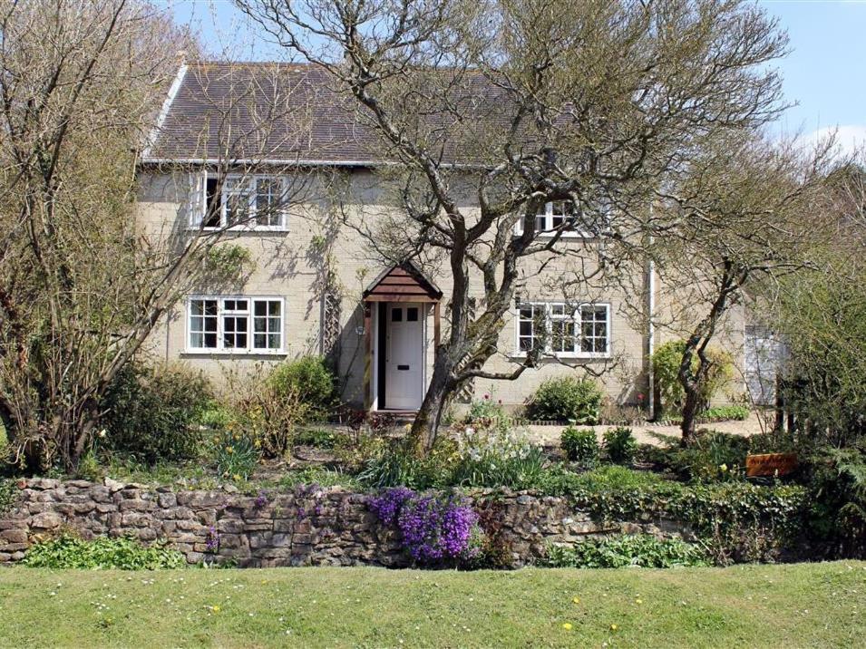 a white house with a stone wall and a tree at Winterbourne Cottage in Chilmark