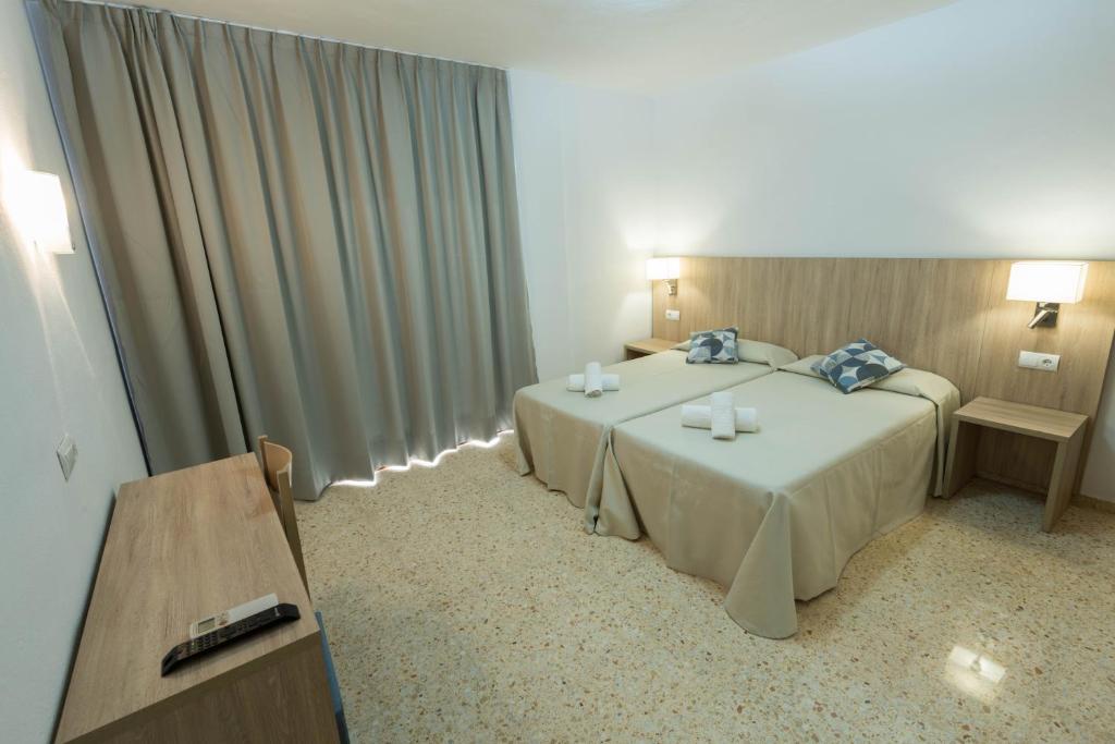 Habitación de hotel con 2 camas y mesa en Hostal Mayol en Santa Eulalia del Río