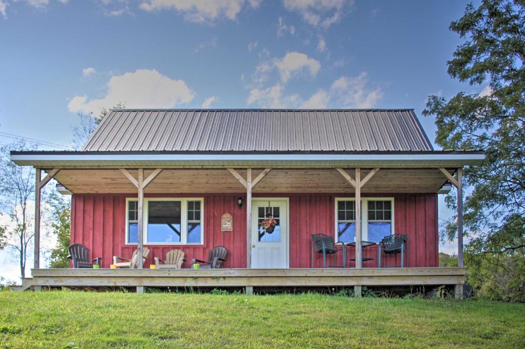 a red house with a porch and chairs in a field at Rural Farmhouse Cabin on 150 Private Wooded Acres! in Mayville