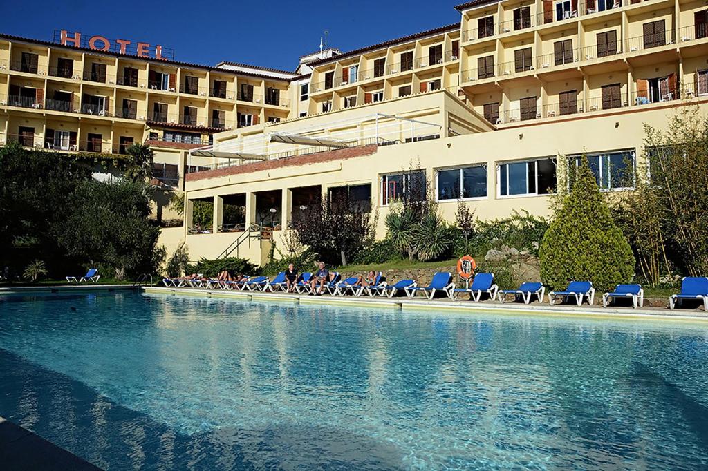 a hotel with a swimming pool with chairs and a building at Hotel Grecs in Roses