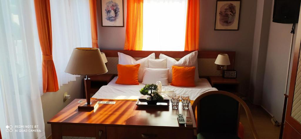 1 dormitorio con cama con almohadas de color naranja y escritorio en Hermina Panzió, en Siófok