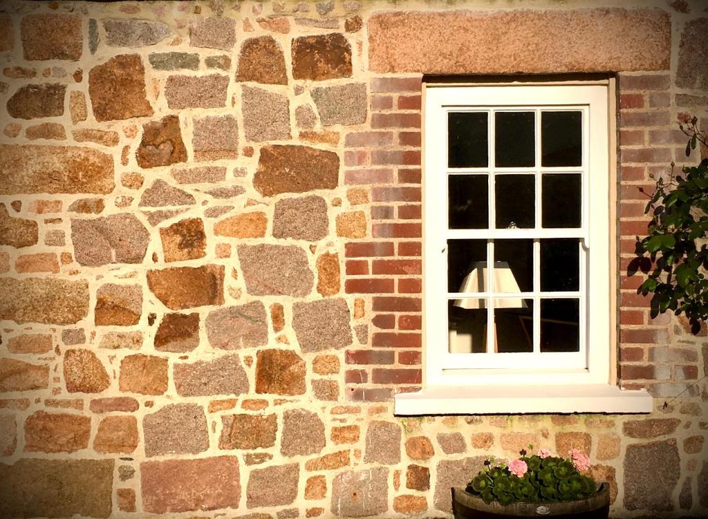 Peaceful 2 bedroom granite country dower house في La Villaise: نافذة من مبنى من الطوب مع نبات الفخار
