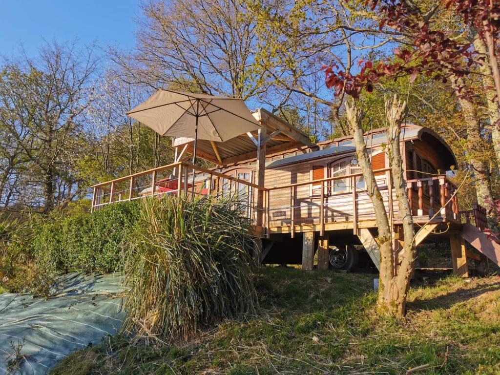 una casa en el árbol con porche y sombrilla en La roulotte de Fichous, en Fichous-Riumayou