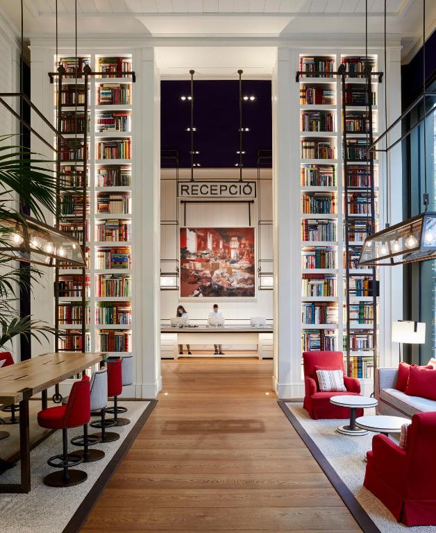 a library with red chairs and a table and bookshelves at Seventy Barcelona in Barcelona