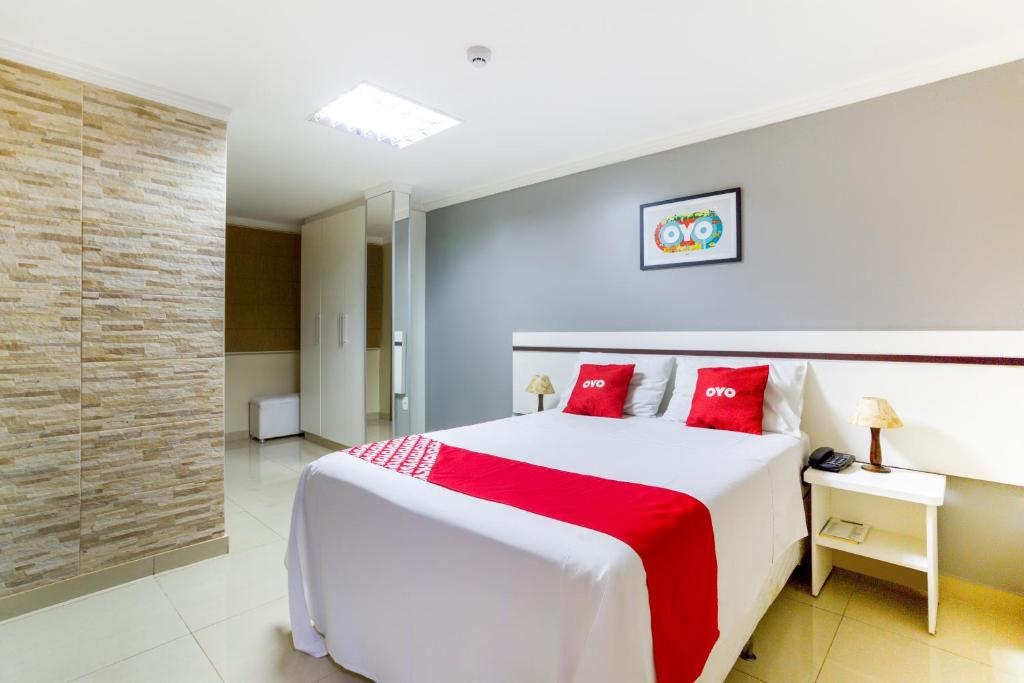 1 dormitorio con 1 cama blanca grande con almohadas rojas en OYO Hotel Via Universitária, Anápolis, en Anápolis