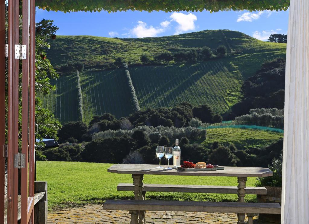 a picnic table with wine glasses and a view of a vineyard at The Vineyard Cottage in Onetangi