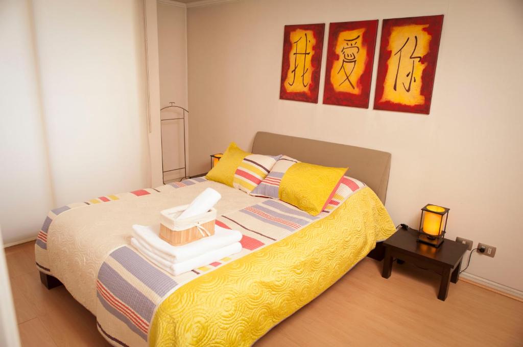 1 dormitorio con 1 cama con sábanas amarillas y pinturas en Chilean Suites Providencia, en Santiago