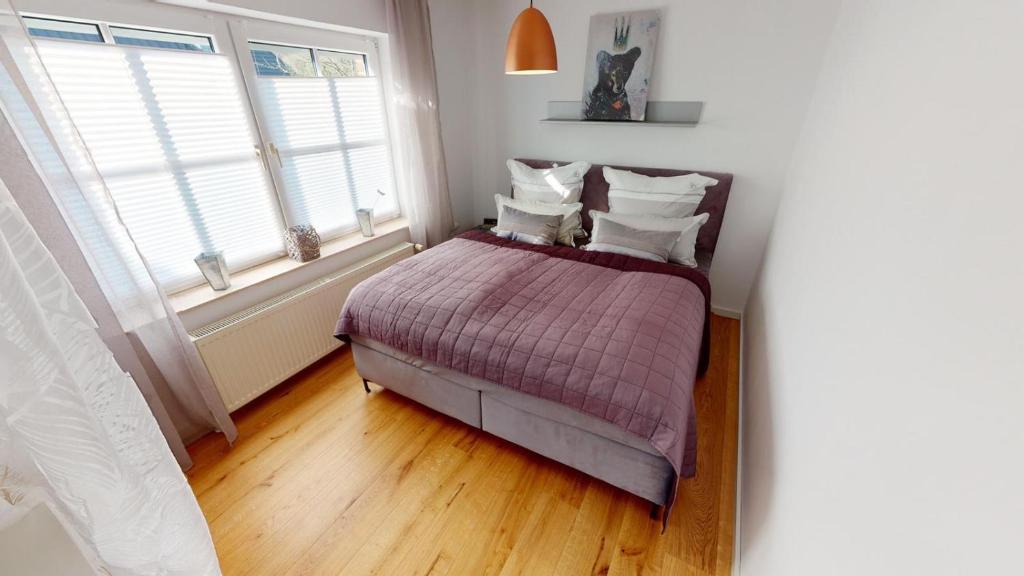 a bedroom with a bed with a purple comforter and two windows at Ferienwohnung Sonnenschein in Goslar