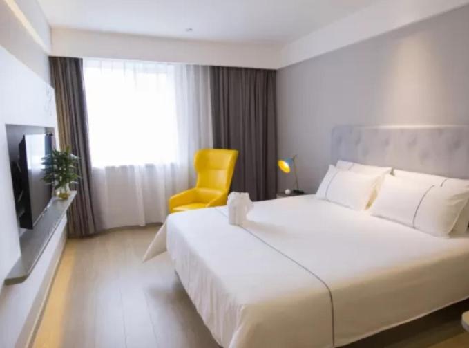 a bedroom with a large white bed and a yellow chair at Magnotel Wenzhou Wu-ma street hotel in Wenzhou