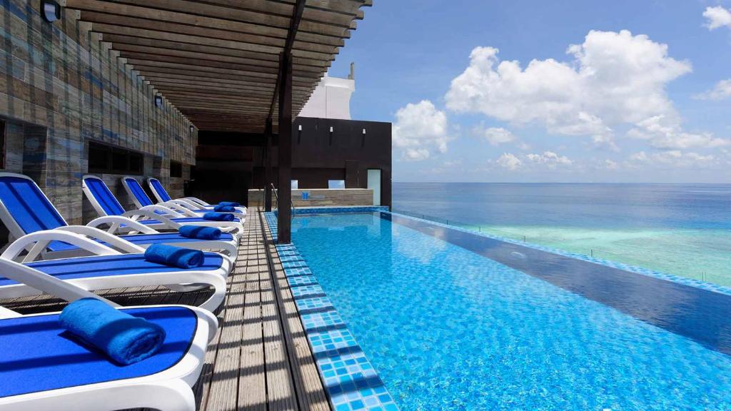 a swimming pool with blue and white chairs next to the ocean at Arena Beach Hotel in Maafushi
