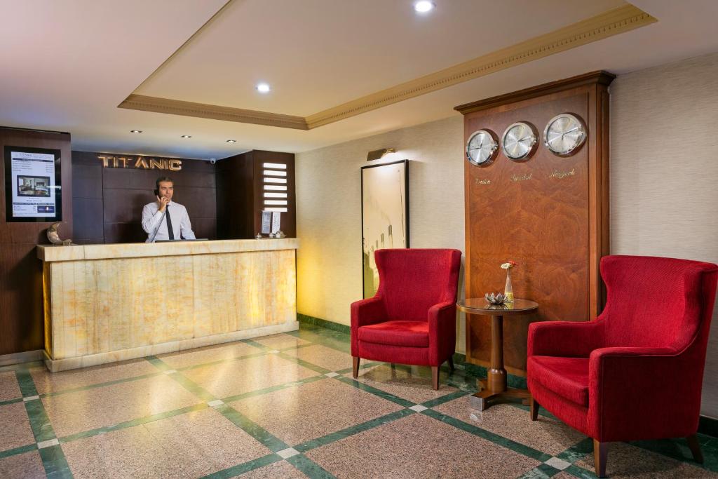 a lobby with two red chairs and a man standing at a counter at Titanic Comfort Sisli in Istanbul