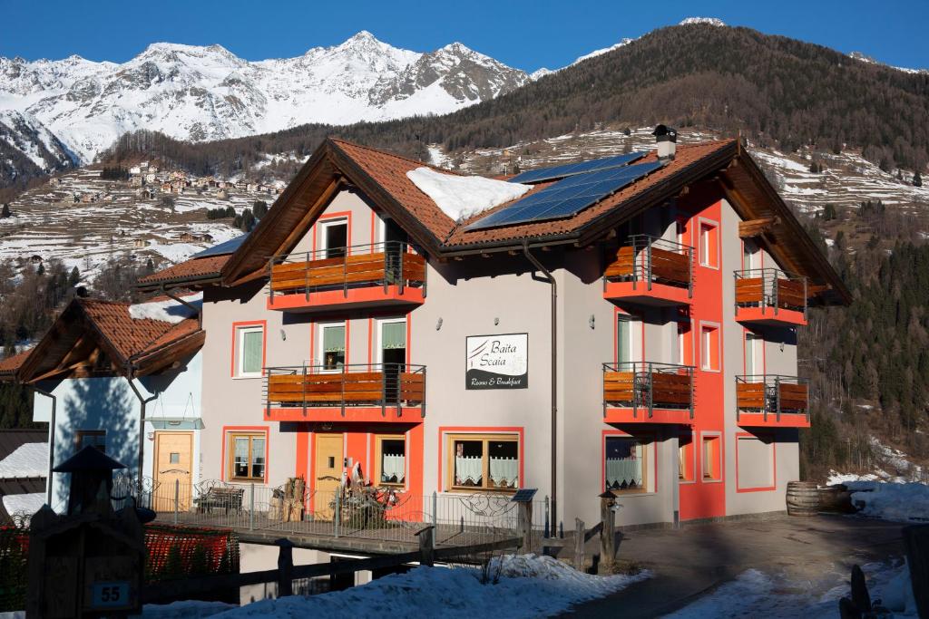 ein Gebäude mit orange und weiß mit verschneiten Bergen in der Unterkunft Baita Scaia in Cogolo