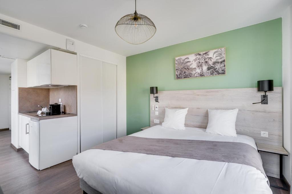 パレゾーにあるAll Suites Appart Hôtel Massy Palaiseauの緑の壁のベッドルーム1室(大きな白いベッド1台付)