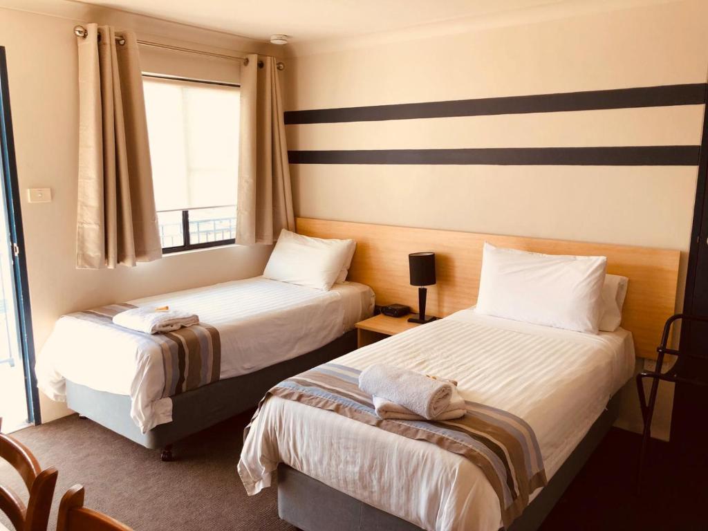 Habitación de hotel con 2 camas y ventana en Red Cedar Motel en Muswellbrook
