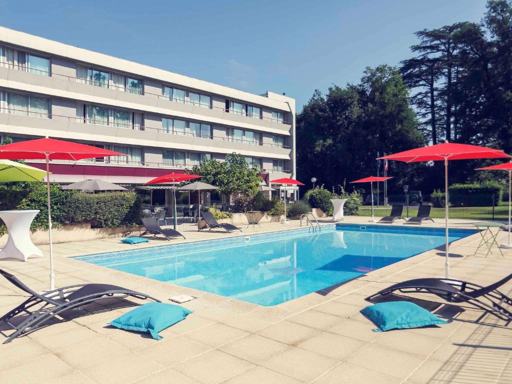 una piscina con sillas y sombrillas frente a un hotel en Mercure Brive, en Ussac